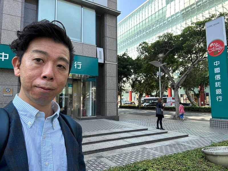 台湾現地法人の資本金口座を開設した銀行前に立つ佐藤大介