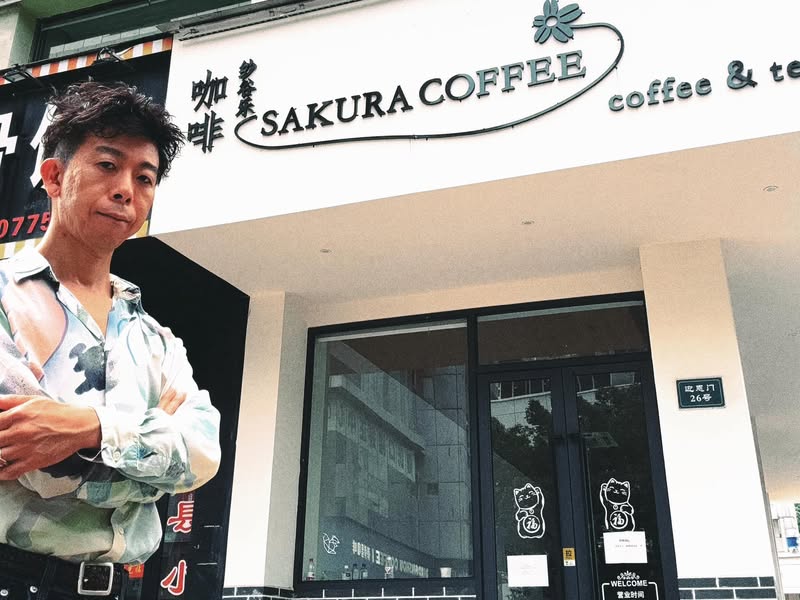 Sakura Coffeeの看板の前に立つ佐藤大介