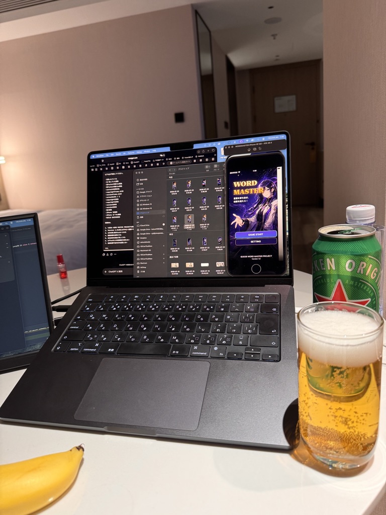 ビールを置いたホテルの机でWORD MASTERのタイトル画面と素材一覧を確認するノートパソコン